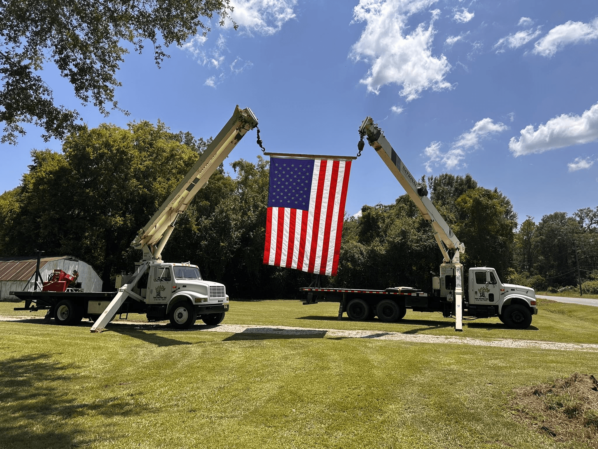 Two TB Tree Service crane trucks holding an American flag between their extended booms